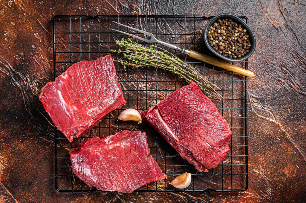 Raw Wild Game Meat of Venison dear ready for cooking. Dark background. Top view