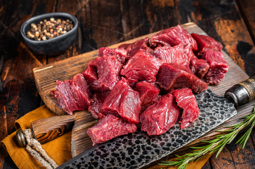 Sliced Raw venison dear meat for a stew, game meat on butcher cutting board. Wooden background. Top view